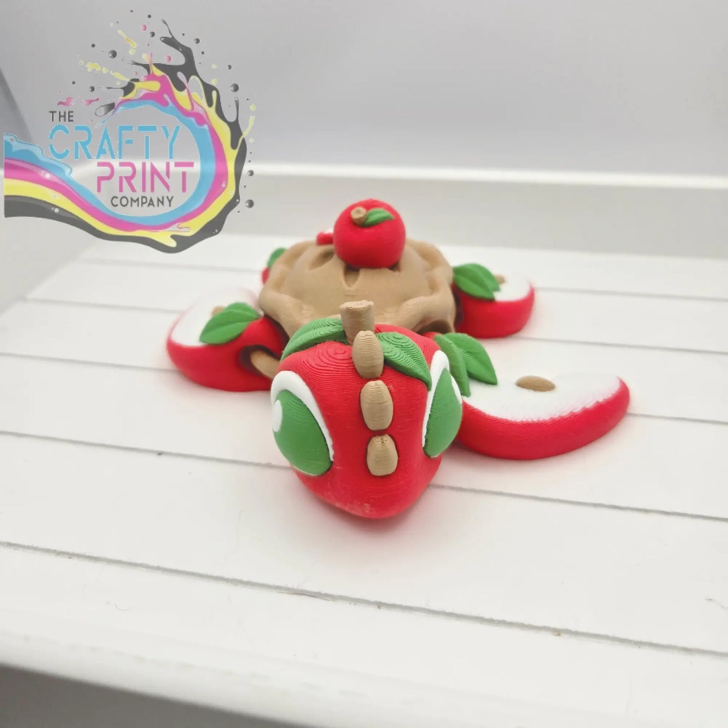 A whimsical red clay apple-shaped sea turtle flexi fidget toy with green eyes and leafy appendages