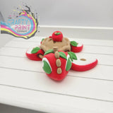 A whimsical red clay apple-shaped sea turtle flexi fidget toy with green eyes and leafy appendages