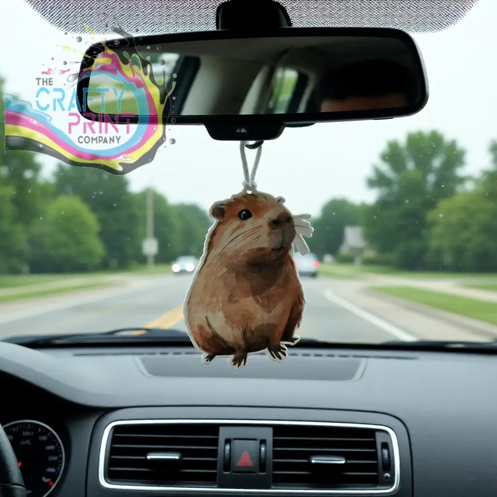 A brown capybara shaped car air freshener hanging from a rearview mirror for a fresh car interior