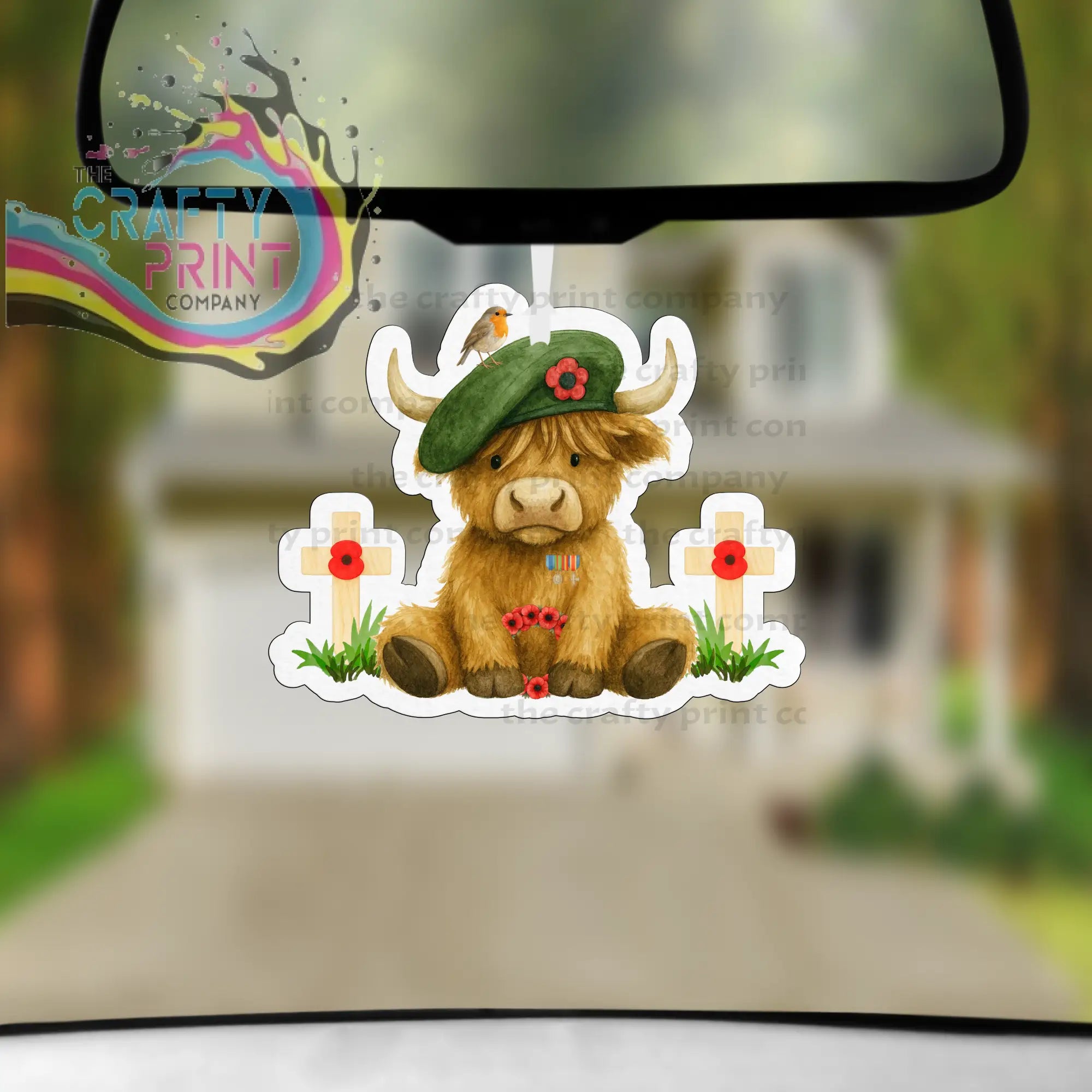Cute brown highland cow car air freshener wearing a green beret with red poppies beside remembrance crosses in grass