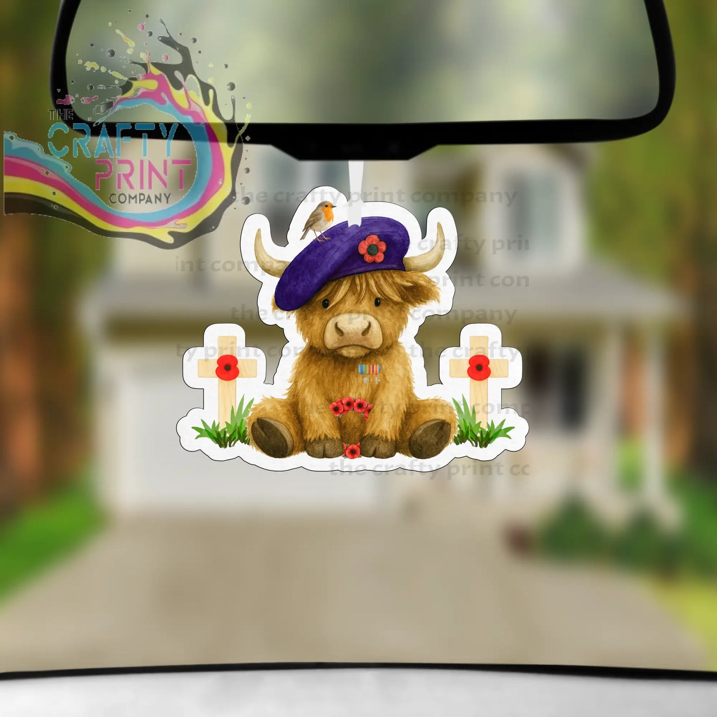 A brown highland cow car air freshener with a purple beret and red poppy between white crosses with poppies