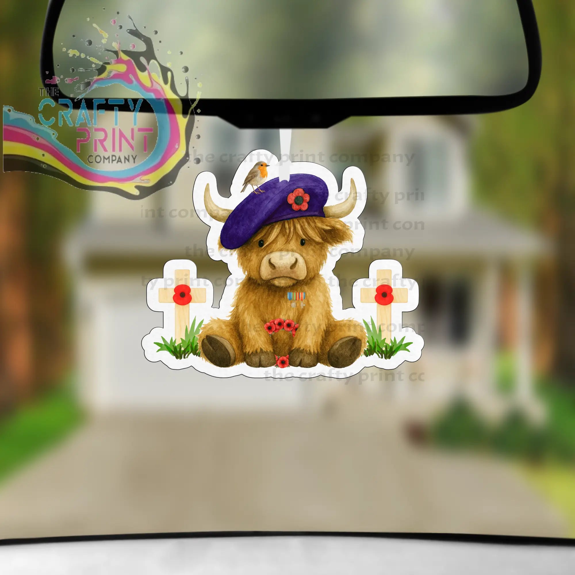 A brown highland cow car air freshener with a purple beret and red poppy between white crosses with poppies