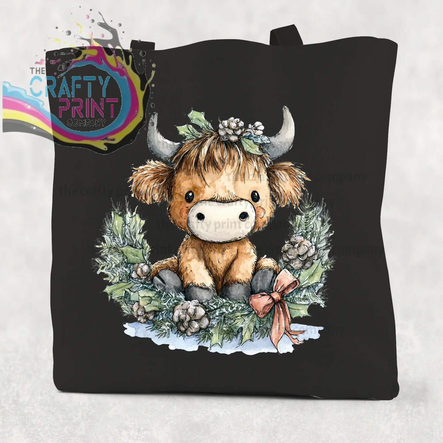 Black cotton tote bag featuring a highland cow wreath watercolor illustration with silver horns and festive holly design