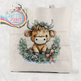 Beige cotton tote bag featuring a highland cow wreath watercolor illustration with silver horns and festive holly accents