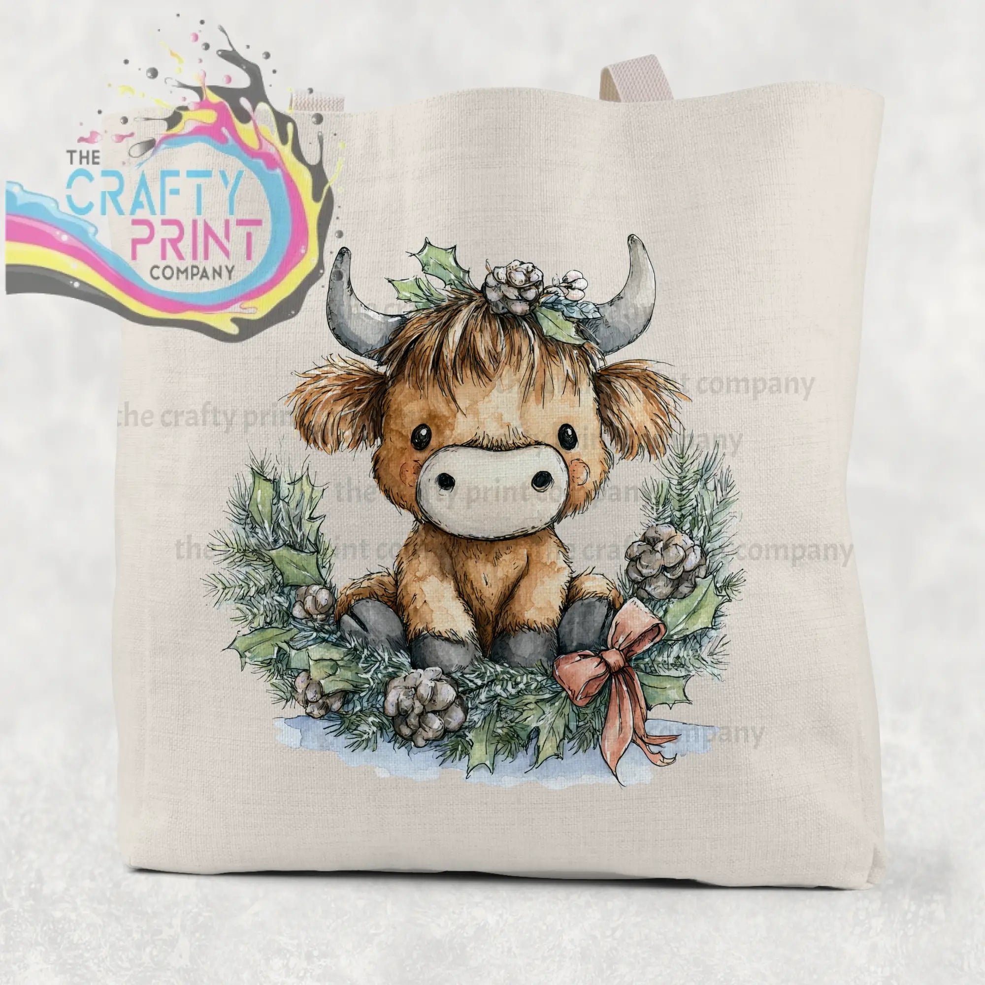 Beige cotton tote bag featuring a highland cow wreath watercolor illustration with silver horns and festive holly accents