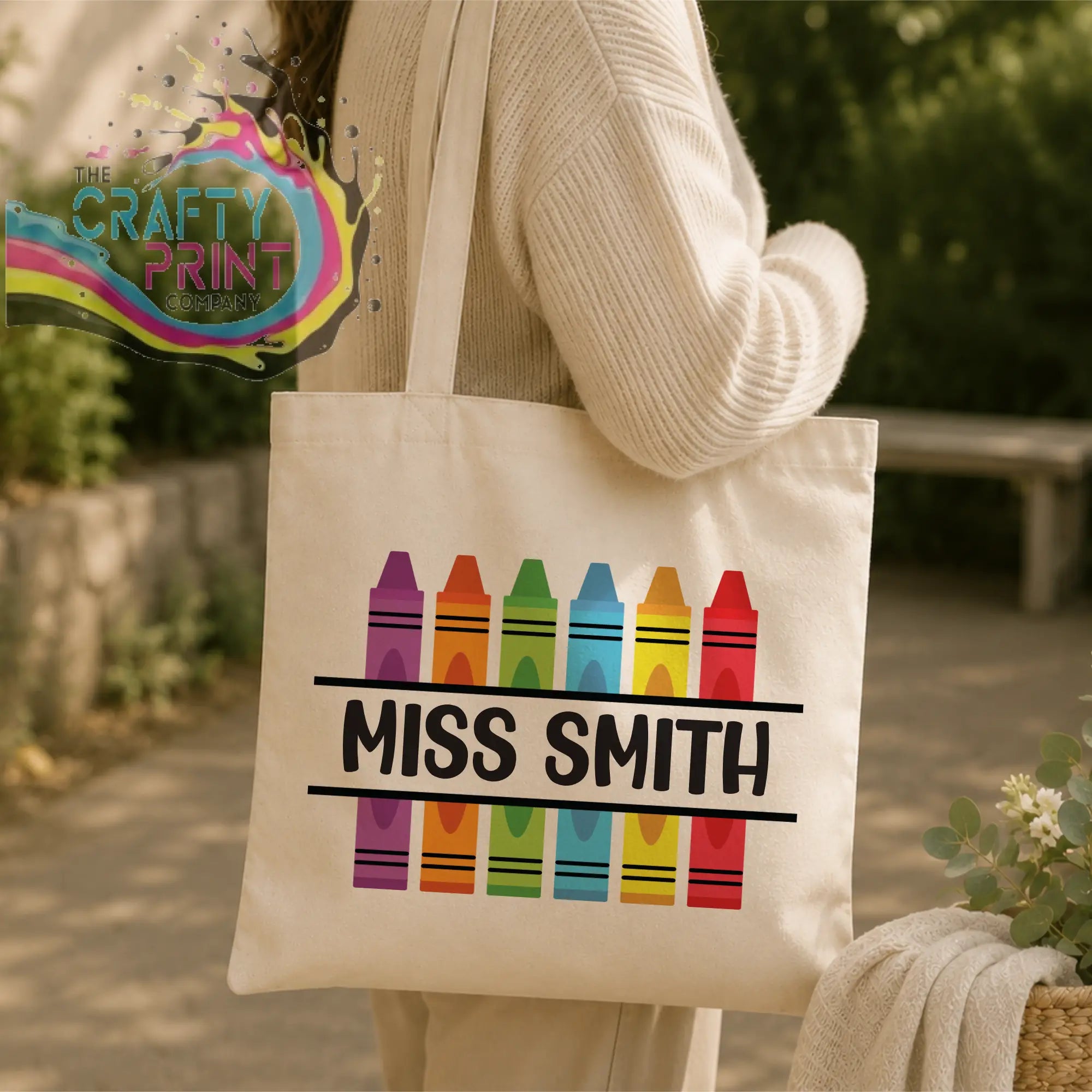 Cream-colored canvas personalised crayon teacher tote bag with colorful rainbow crayon design and miss smith text