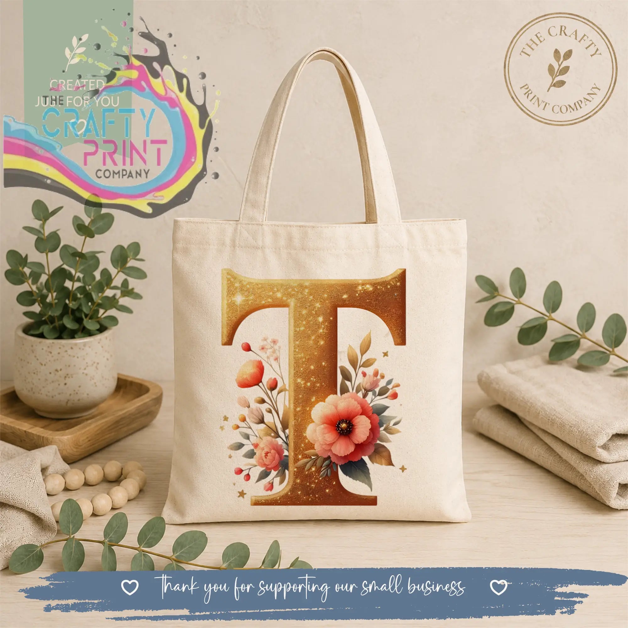 Cream-colored canvas tote bag featuring a gold glitter initial t with delicate pink and orange floral illustrations