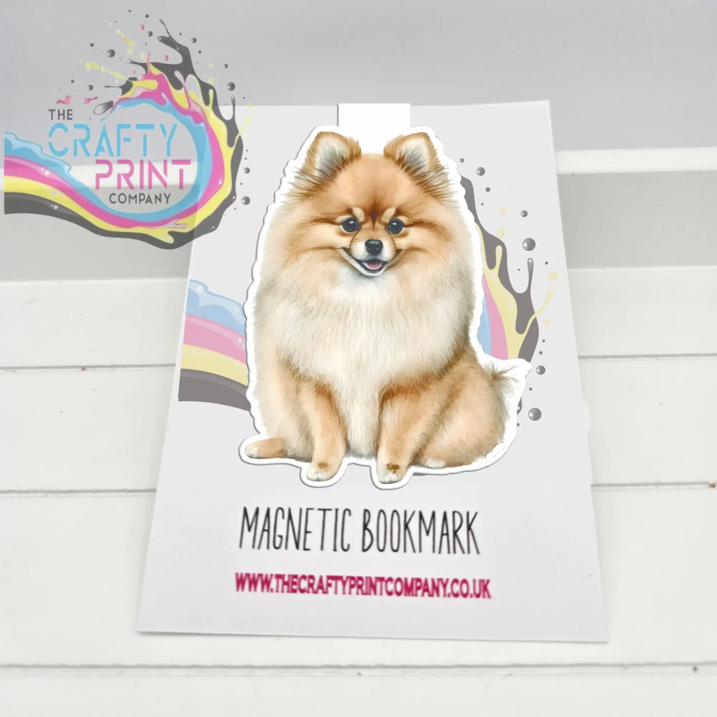 A charming fluffy pomeranian magnetic bookmark with colorful splatter accents on a white background