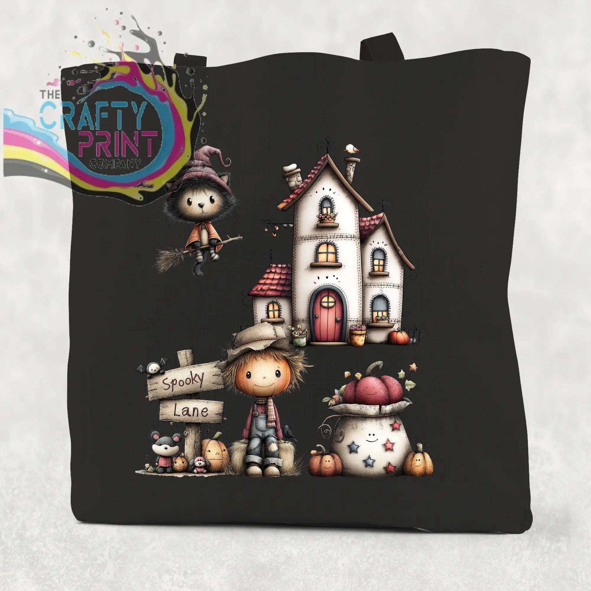 Black cotton re-usable tote bag with spooky lane halloween design featuring witch cat, scarecrow, and pumpkin house