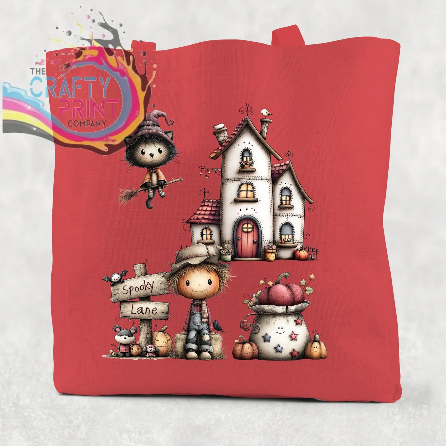 Red cotton re-usable tote bag featuring a spooky lane halloween illustration with witch cat haunted house and scarecrow