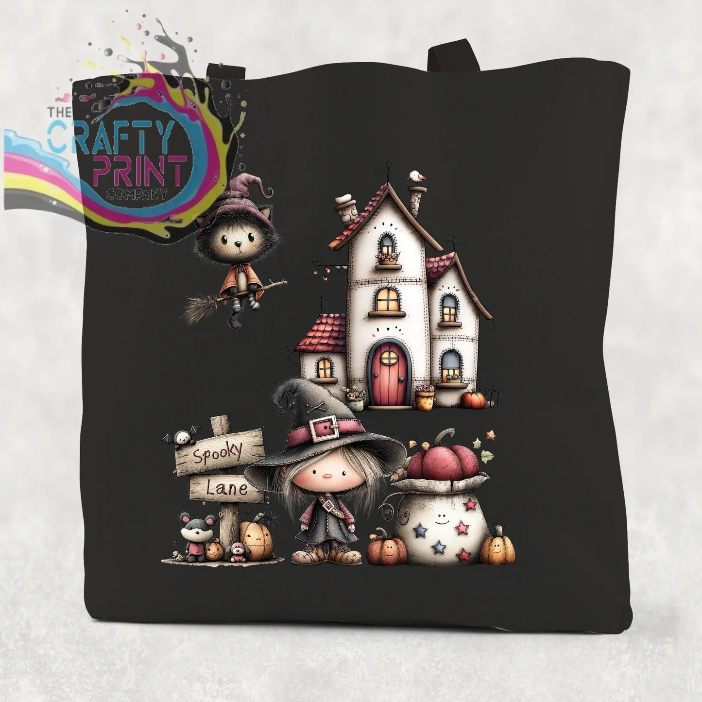 Black cotton re-usable tote bag featuring a whimsical spooky lane halloween scene with witches pumpkins and a house
